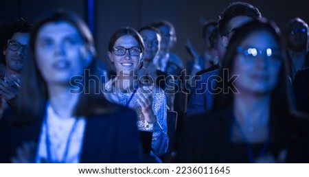 Attractive Female Sitting in a Dark Crowded Auditorium at a Tech Conference. Young Woman Applauding After a Successful Keynote Presentation. Specialist Inspired by Latest Technological Advances. Royalty-Free Stock Photo #2236011645