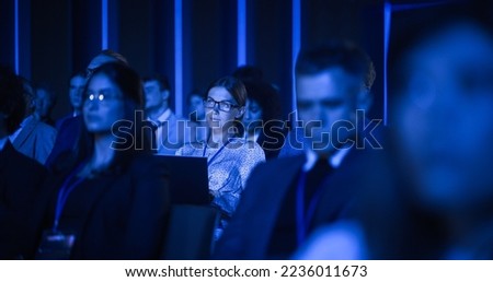 Young Woman Sitting in a Crowded Audience at a Business Conference. Female Delegate Using Laptop to Take Notes. Manager Watching Inspirational Entrepreneurship Presentation About Developing Markets. Royalty-Free Stock Photo #2236011673