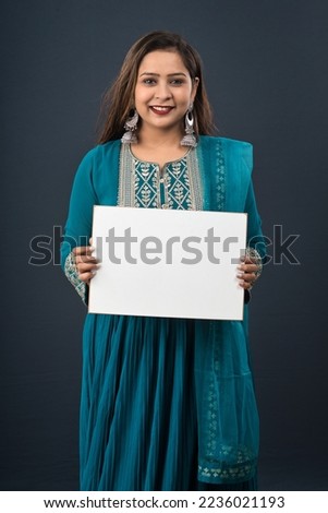 A young girl or woman wearing an Indian traditional dress holding a signboard in her hands on gray background.