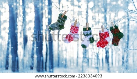 colorful knitted wool socks hanging on wooden clothespins against winter natural forest background. symbol of Festive Winter season. Christmas, new year holidays. cold snowy weather. copy space