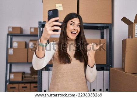 Young brunette woman working at small business ecommerce taking selfie pointing thumb up to the side smiling happy with open mouth 
