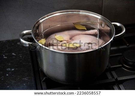 Raw chicken legs in water with herbs in a big stainless steel pot