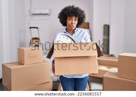 Black woman with curly hair moving to a new home holding cardboard box skeptic and nervous, frowning upset because of problem. negative person. 