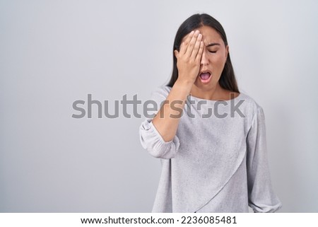 Young hispanic woman standing over white background yawning tired covering half face, eye and mouth with hand. face hurts in pain. 