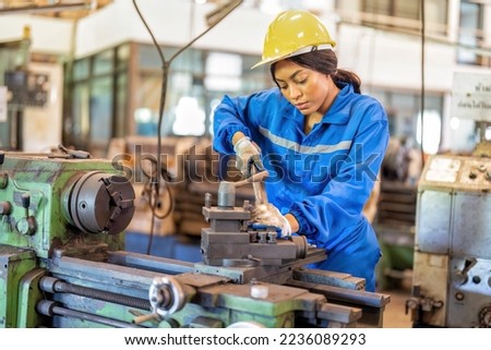Woman worker in uniform operating machine at factory concentrate on fabrication job on lathe