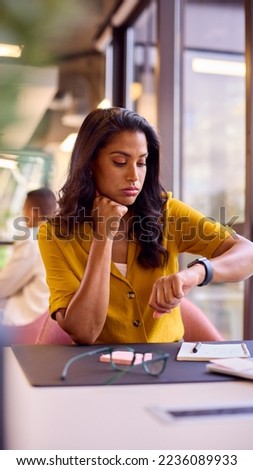 Bored Mature Businesswoman Working At Desk In Office Looking At Watch