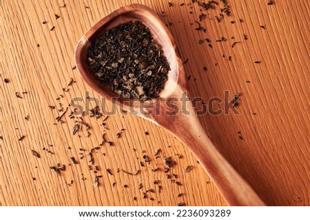 Wooden spoon and scattered black dry tea grain on the kitchen table. Food and drink theme, top view