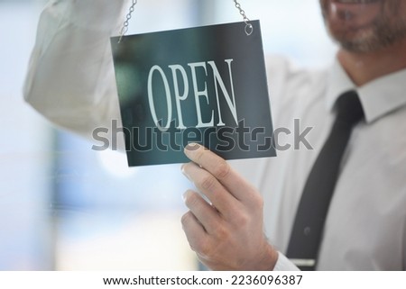 Businessman, advertising open sign and window in office of new business, company or startup agency. Closeup of executive hanging signage for opening day at glass display, announcement and information