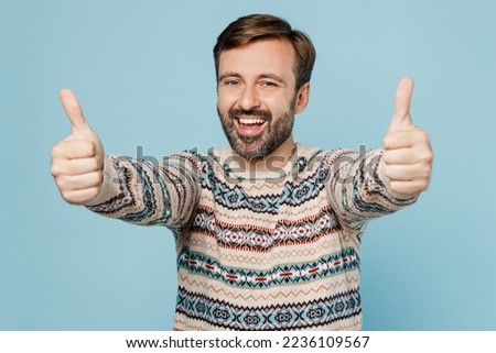 Young smiling happy satisfied cheerful fun caucasian man 30s he wear sweater showing thumb up like gesture isolated on plain pastel light blue cyan background studio portrait. People lifestyle concept