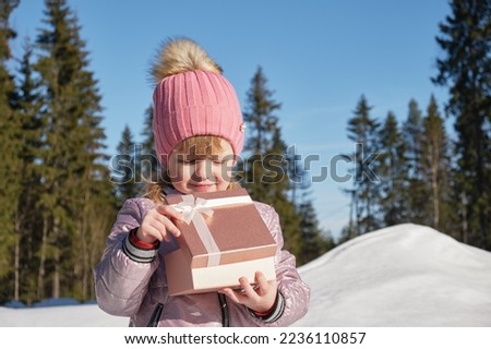 preschool girl with shiny gift box outside, winter day , sunny and cold weather, christmas present concept