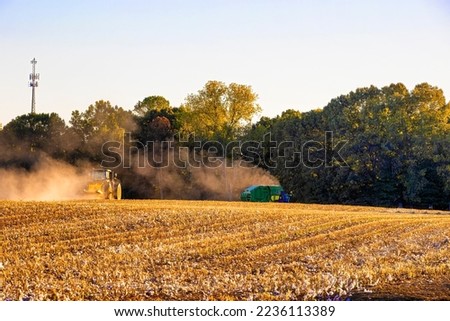 Rural Arkansas, USA - October 1, 2022:  A John Deere tractor travels back across a cotton stubble field towards the harvester to pick up another round bail of cotton.