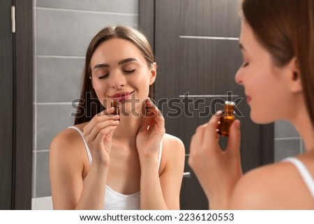 Young woman smelling essential oil in bathroom Royalty-Free Stock Photo #2236120553