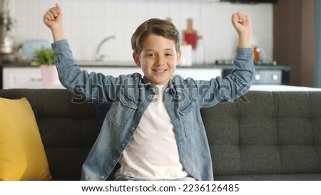 Little boy showing his joy to the camera on the sofa at home. The boy is very happy with the news he receives. Concept of celebrating success. Smiling emotions, happy childhood.