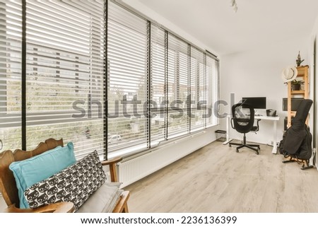 a living room with wood flooring and white shutters on the windows looking out onto an office desk area Royalty-Free Stock Photo #2236136399
