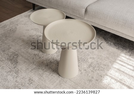 Modern living room interior with light grey carpet and two round textured metal coffee tables of different sizes