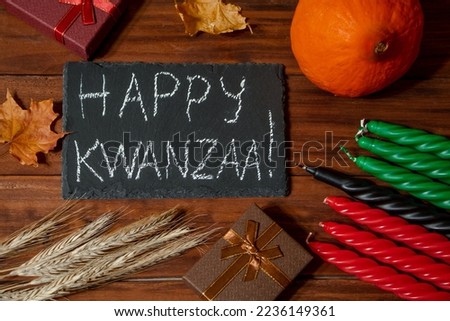 Kwanzaa African American holiday. Seven candles red, black and green on a natural wooden background. Symbols of African heritage. Congratulatory inscription and gifts.