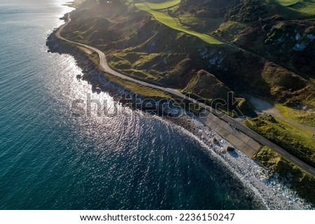 Causeway Coastal Route a.k.a Antrim Coast Road A2 on the Atlantic coast in Northern Ireland. One of the most scenic coastal roads in Europe. Aerial view against the rising sun in winter Royalty-Free Stock Photo #2236150247