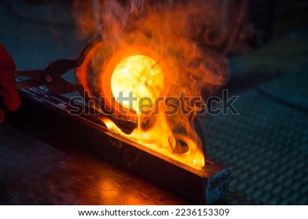 The master's hands in special red refractory mittens pour molten gold from a refractory glass into a mold. Royalty-Free Stock Photo #2236153309