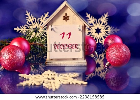 Calendar for December 11: decorative house with the name of the month December, numbers 11, pink Christmas balls, decorative snowflakes on a blue background, bokeh