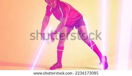 Low section of african american rugby player holding ball by glowing lights over beige background. Illuminated, copy space, composite, sport, competition, playing, match, line and abstract concept.