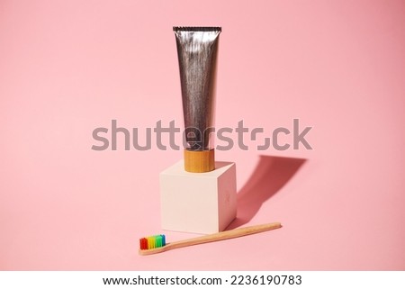 A tube of toothpaste and a wooden brush on a pink background. Empty space for text. Self-care concept.