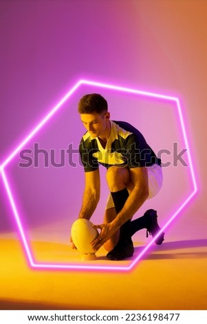 Caucasian male rugby player placing ball on stand by illuminated hexagon over gradient background. Copy space, composite, sport, shape, competition, playing, match and abstract concept.