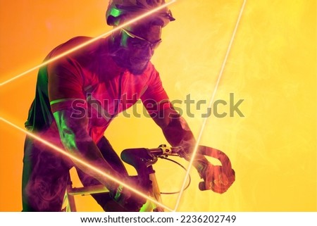 African american male athlete wearing helmet and eyewear riding bike by illuminated triangle. Copy space, composite, sport, cycling, racing, competition, yellow, shape and abstract concept.
