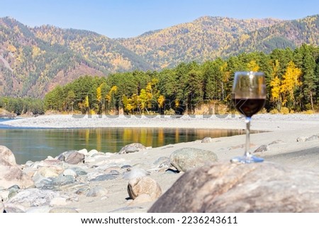 glass of red wine in blur. autumn mountains, river surface of mountain river, natural background, relaxation and travel concept. Reflection of autumn in glass. winemaking concept, selective focus