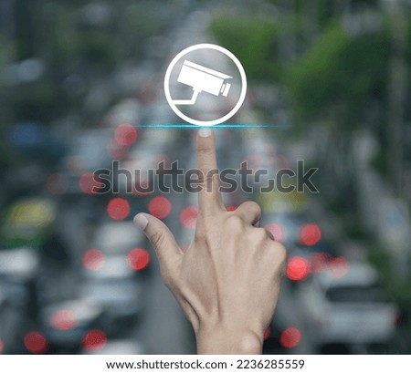 Hand pressing cctv camera flat icon over blur of rush hour with cars and road in city, Technology security and safety online concept