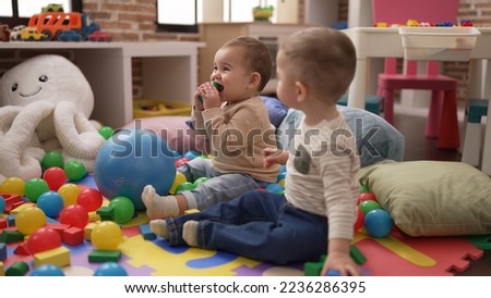 Two adorable toddlers sitting on floor sucking construction block at kindergarten Royalty-Free Stock Photo #2236286395