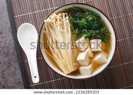 Enoki Miso Soup with tofu cheese and seaweed close-up in a bowl on the table. Horizontal top view from above
