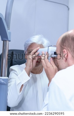 Attractive male ophthalmologist is checking eye vision of middle aged woman in modern clinic, doctors and ophthalmology clinic patients.