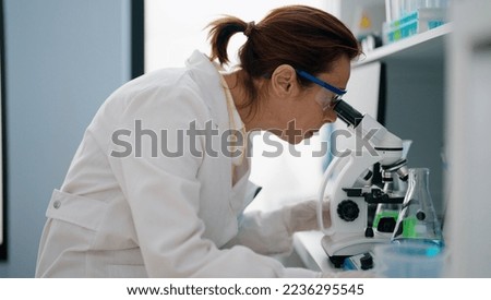 Middle age hispanic woman wearing scientist uniform using microscope at laboratory