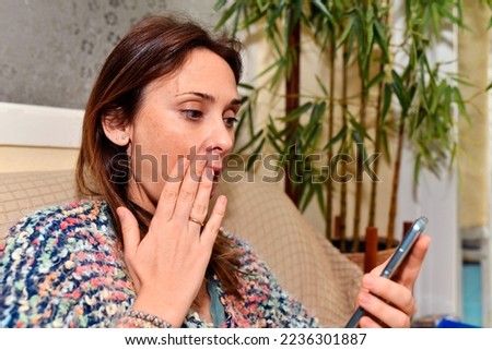 woman at home sitting on sofa showing surprise while looking at smartphone Royalty-Free Stock Photo #2236301887