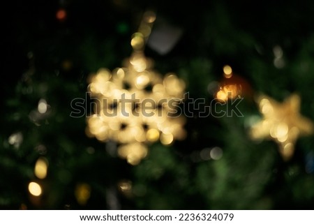 Blurry golden, sparkling Christmas tree ornament in shape of snowflake star with glitter, beautiful glowing bokeh effect with shimmering lights, dark green background, abstract image for holiday card
