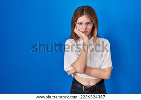 Beautiful woman standing over blue background thinking looking tired and bored with depression problems with crossed arms. 