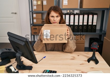 Young beautiful woman working at small business ecommerce holding box skeptic and nervous, frowning upset because of problem. negative person. 