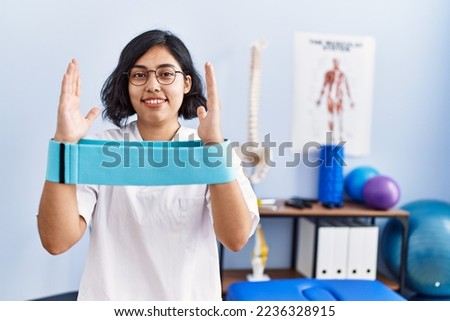 Young latin woman wearing physiotherapist uniform holding elastic band at physiotherapy clinic