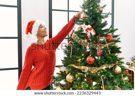 Young hispanic woman smiling confident decorating christmas tree at home