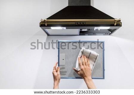 cropped shot of black metal hood extractor and person hand holding and cleaning aluminum mesh filter on white wall background, housework concept Royalty-Free Stock Photo #2236333303