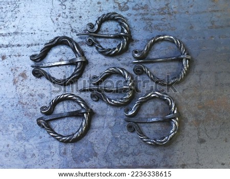 6 metal forged twisted brooches in one photo, lying against the background of a sheet of metal. Fibula - an ancient element of the costume