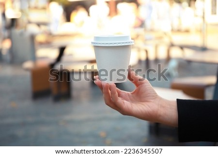 Woman holding cardboard cup with coffee on city street, closeup. Space for text