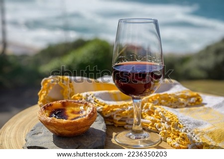 Portugal's traditional food and drink, glass of porto wine and sweet dessert Pastel de nata egg custard tart pastry served with view on blue Atlantic ocean near Sintra in Lisbon area, Portugal