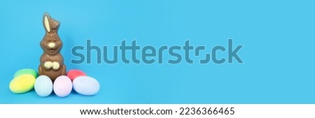 Banner. Easter Chocolate Bunny and eggs are plain, multi-colored on a blue background. Holiday concept, gifts, customs, copy space, text, template, poster, business,congratulations, invitation,action.