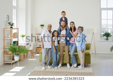 Happy family poses for the camera in a large bright cozy room. The son is on the shoulders of the father, the daughter, the spouse and the parents are nearby. Happy relationships in a large family. Royalty-Free Stock Photo #2236385323
