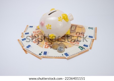 Piggy bank on top of fifty euro banknotes with one and tow euros coins, on a white background. Top view. Concept of saving money. copy space.