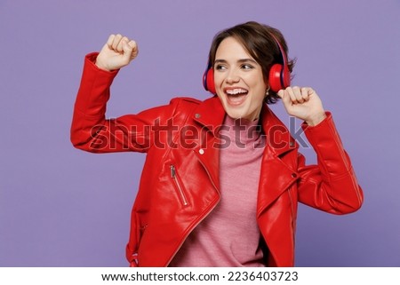 Young smiling happy cheerful cool woman 20s wear red leather jacket headphones listen to music dance isolated on plain pastel light purple background studio portrait. People lifestyle fashion concept