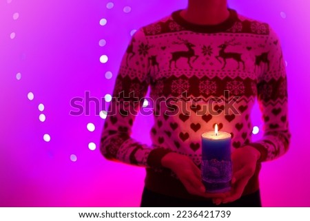 Woman holding christmas candle with christmas trees. She is wearing a Christmas sweater with reindeers. Picture in pink and purple tones - refers to Christmas.                               