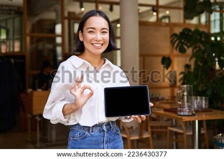 Enthusiastic asian woman shows okay sign, tablet screen, looks impressed, recommends smth. Copy space