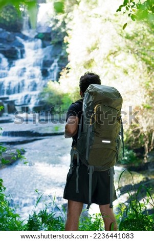 

young man walking with a travel backpack looks at the view towards the waterfalls in front of him